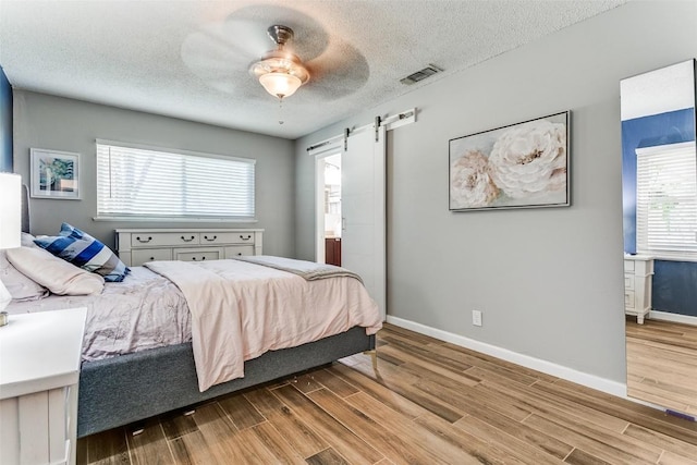 bedroom featuring a barn door, baseboards, multiple windows, and wood finished floors