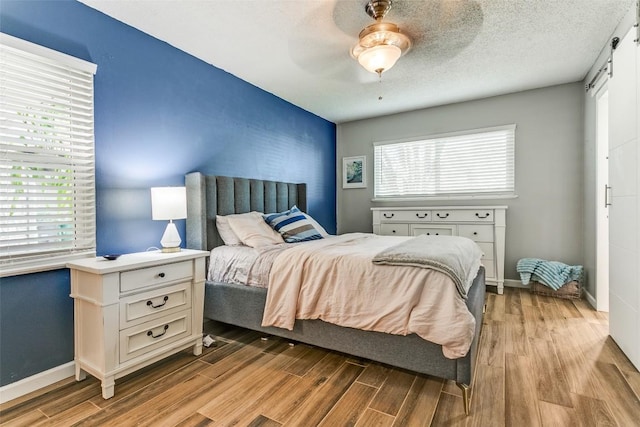 bedroom featuring light wood finished floors, a barn door, baseboards, an accent wall, and a ceiling fan