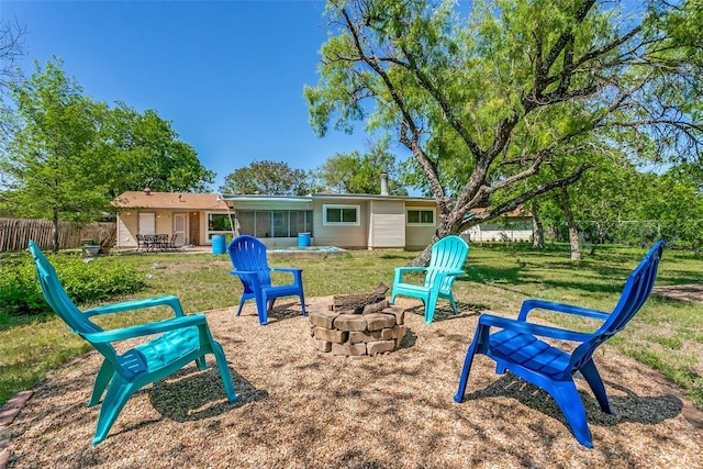exterior space featuring fence, a patio area, a lawn, a sunroom, and an outdoor fire pit