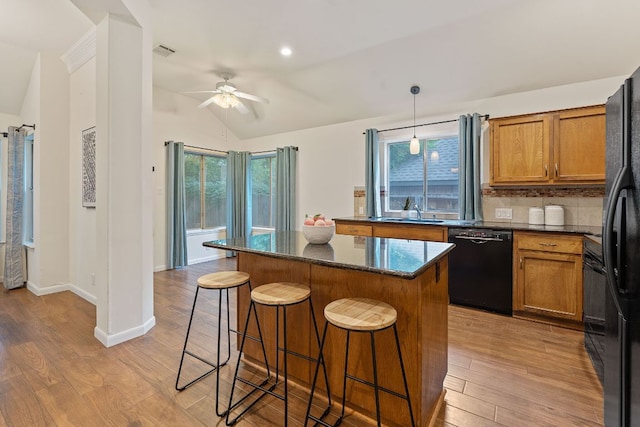 8104 Isaac Pryor Dr, Austin, TX 78749 - kitchen featuring brown cabinetry, black appliances, a breakfast bar area, lofted ceiling, and a kitchen island