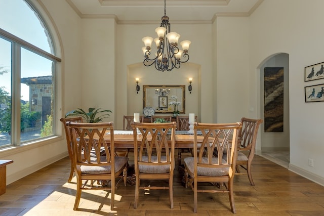 dining area with an inviting chandelier, a towering ceiling, ornamental molding, and wood-type flooring