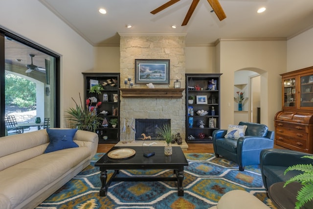 living area featuring arched walkways, wood finished floors, ceiling fan, a fireplace, and ornamental molding