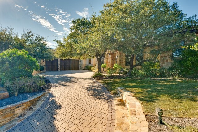 obstructed view of property featuring a gate, fence, decorative driveway, and a front yard