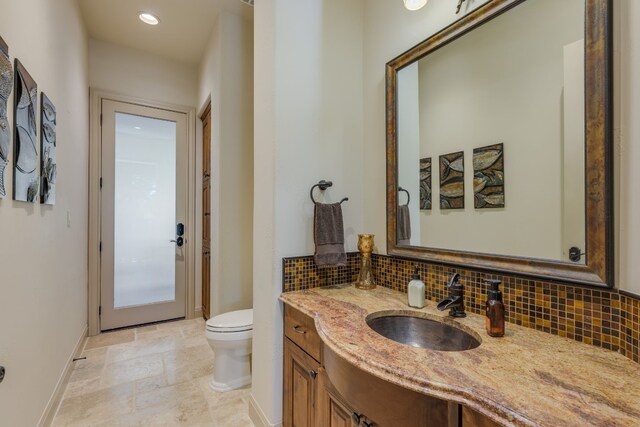 bathroom featuring decorative backsplash, stone tile flooring, vanity, and toilet
