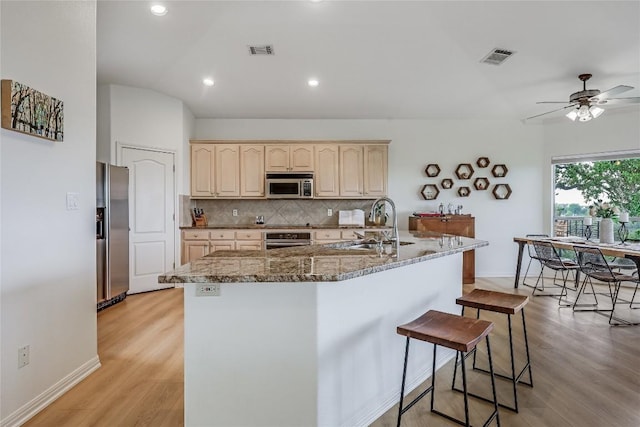 20718 Camel Back St, Lago Vista, TX 78645 - kitchen featuring stainless steel appliances, light brown cabinetry, decorative backsplash, a kitchen breakfast bar, and light wood-style flooring