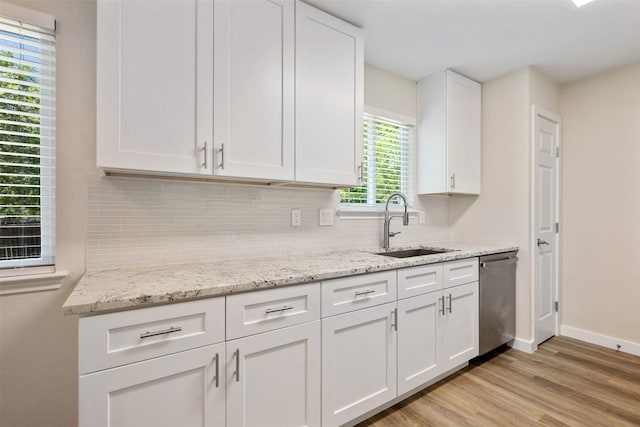 kitchen featuring dishwasher, tasteful backsplash, a sink, and light wood-type flooring