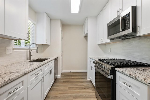 kitchen with backsplash, white cabinetry, stainless steel appliances, and a sink