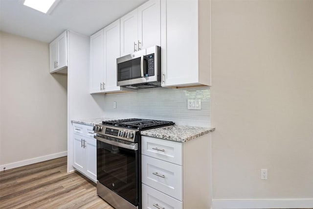 kitchen with light wood-type flooring, baseboards, backsplash, light stone counters, and appliances with stainless steel finishes