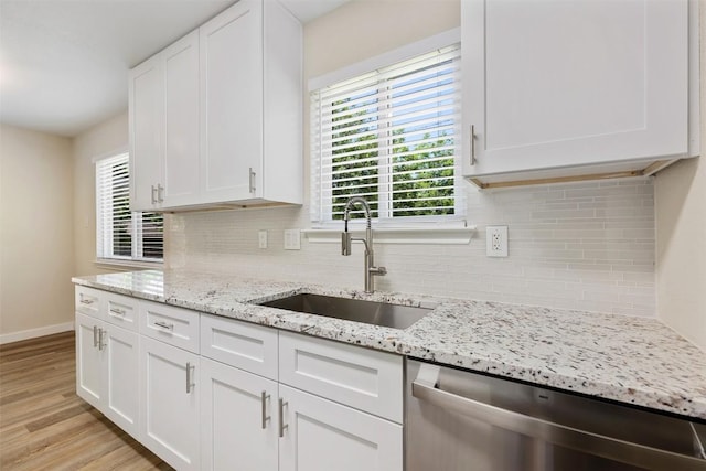 kitchen with white cabinets, stainless steel dishwasher, a sink, light wood-style floors, and decorative backsplash