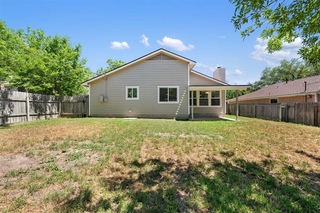 back of house with a patio area, a lawn, a fenced backyard, and a chimney