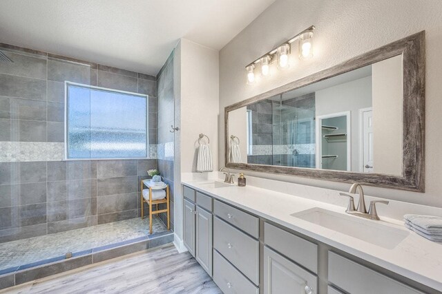 bathroom with wood finished floors, a sink, double vanity, and tiled shower