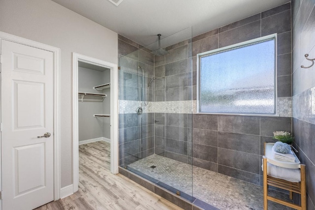 bathroom with a spacious closet, baseboards, walk in shower, and wood finished floors