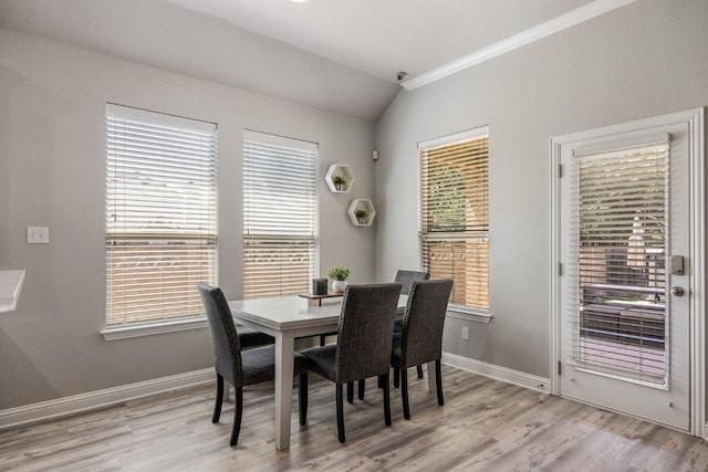 dining space featuring light wood finished floors, ornamental molding, baseboards, and lofted ceiling