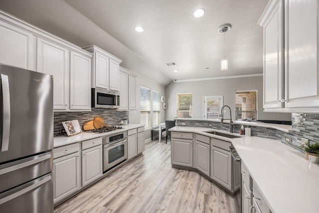 kitchen with a peninsula, a sink, light wood-style floors, gray cabinetry, and appliances with stainless steel finishes