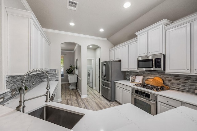 kitchen with a sink, decorative backsplash, arched walkways, washer / dryer, and appliances with stainless steel finishes
