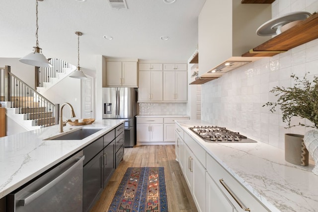 kitchen with stainless steel appliances, open shelves, a sink, light wood-type flooring, and hanging light fixtures