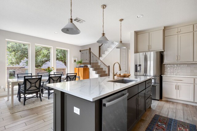 kitchen with stainless steel appliances, light wood-type flooring, backsplash, a sink, and visible vents