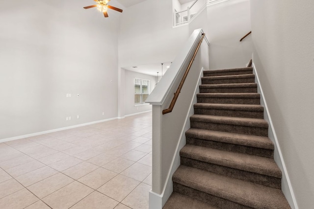 stairway with tile patterned floors, a ceiling fan, a high ceiling, and baseboards