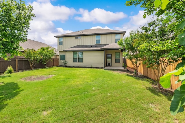 rear view of house with board and batten siding, a fenced backyard, and a yard