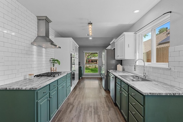 kitchen featuring white cabinets, stainless steel appliances, a sink, green cabinets, and wall chimney range hood