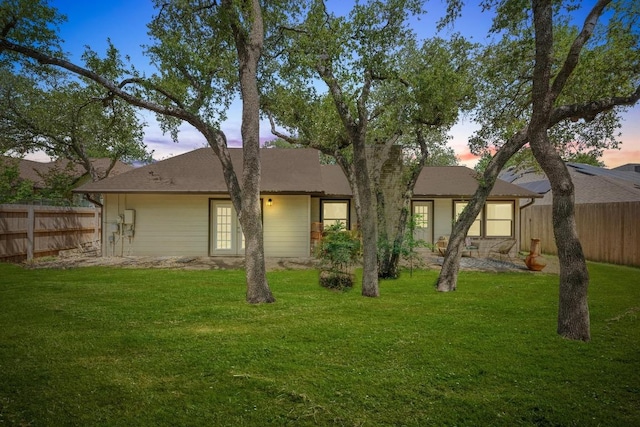 back of property at dusk featuring a lawn and fence