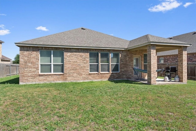 back of house with a fenced backyard, brick siding, a lawn, a shingled roof, and a patio