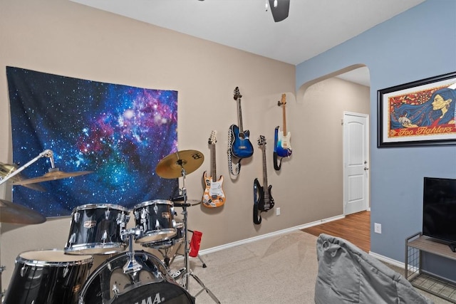 recreation room featuring arched walkways, carpet floors, a ceiling fan, and baseboards