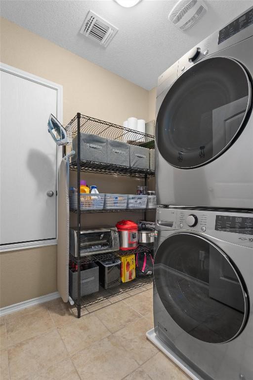 laundry area with tile patterned floors, a textured ceiling, visible vents, stacked washer / drying machine, and laundry area