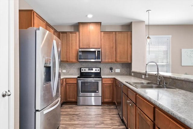 kitchen featuring brown cabinets, light countertops, wood finished floors, a sink, and appliances with stainless steel finishes