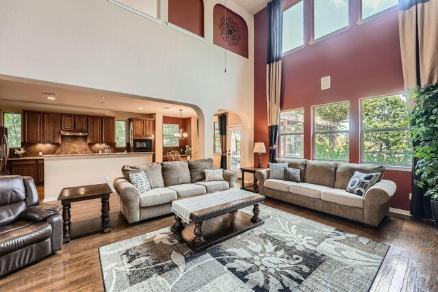 living room with arched walkways, hardwood / wood-style floors, a towering ceiling, and plenty of natural light