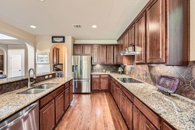 kitchen featuring stainless steel appliances, arched walkways, under cabinet range hood, and a sink