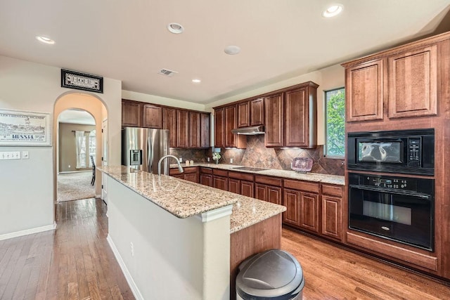 kitchen featuring black appliances, decorative backsplash, a kitchen island with sink, light stone countertops, and visible vents