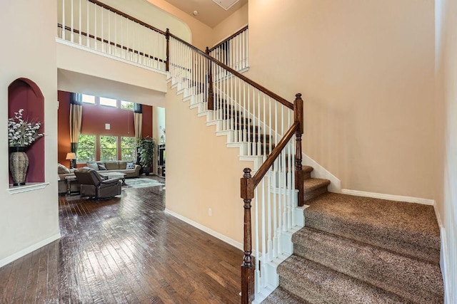 staircase featuring hardwood / wood-style flooring, a high ceiling, and baseboards