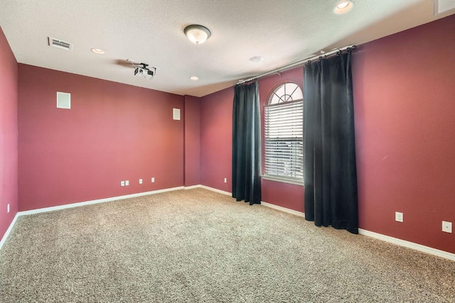 carpeted spare room featuring a textured ceiling, visible vents, and baseboards