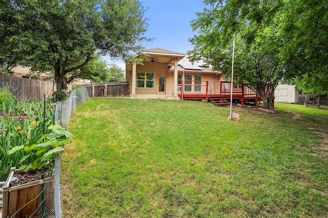 view of yard with a wooden deck, ceiling fan, a shed, a fenced backyard, and an outdoor structure
