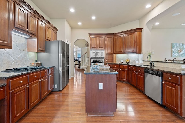 10033 Lisi Anne Dr, Austin, TX 78717 - kitchen featuring appliances with stainless steel finishes, arched walkways, wood finished floors, a center island, and backsplash