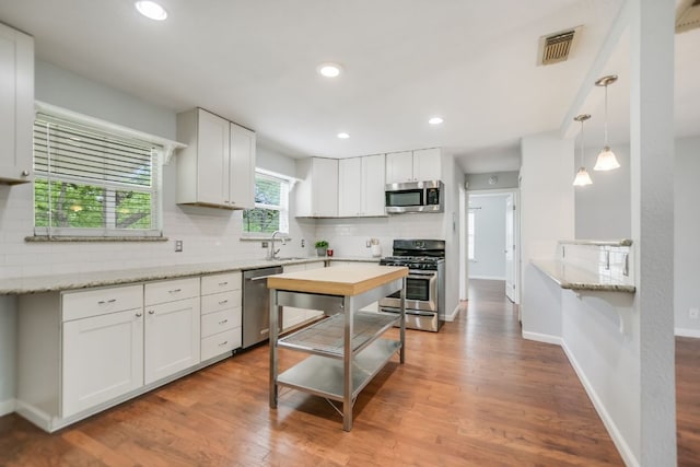kitchen with wood finished floors, decorative backsplash, stainless steel appliances, white cabinetry, and visible vents