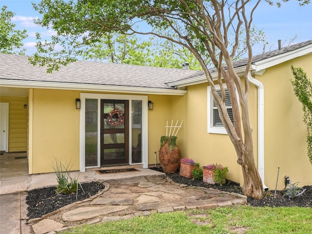 view of exterior entry featuring a shingled roof and stucco siding