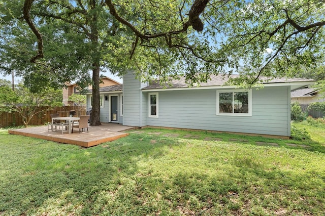rear view of house featuring a wooden deck, a lawn, and fence
