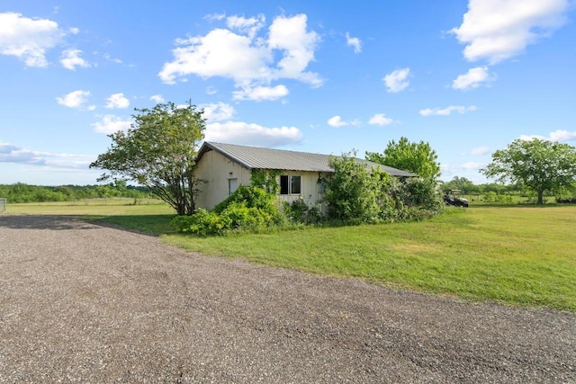 view of property exterior featuring a lawn, dirt driveway, and metal roof