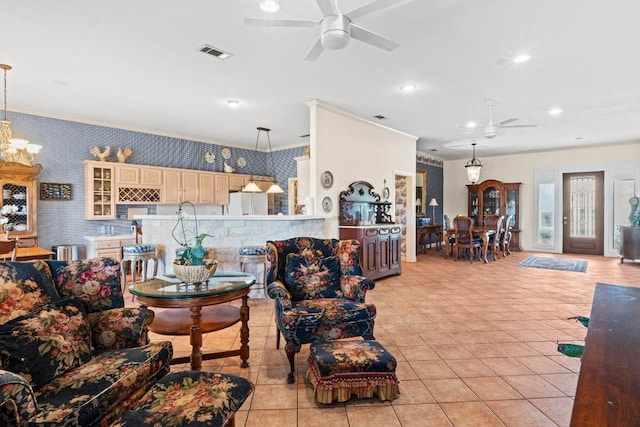 living area featuring ornamental molding, ceiling fan with notable chandelier, wallpapered walls, and visible vents