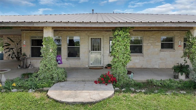property entrance with metal roof, a patio area, and stone siding