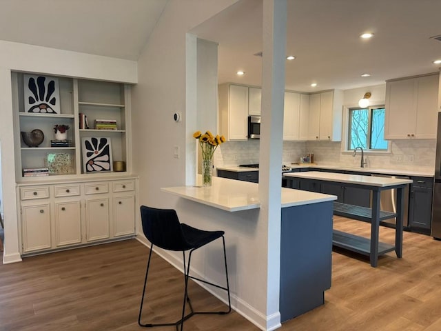 4302 Red Cloud Dr, Austin, TX 78759 - kitchen featuring stainless steel appliances, wood finished floors, white cabinets, decorative backsplash, and a breakfast bar