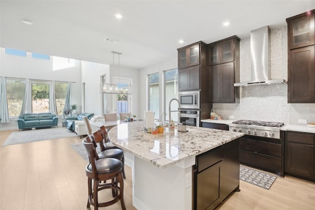 244 Diamondback Dr, Georgetown, TX 78628 - kitchen with wall chimney exhaust hood, appliances with stainless steel finishes, a chandelier, light wood-style flooring, and a center island with sink
