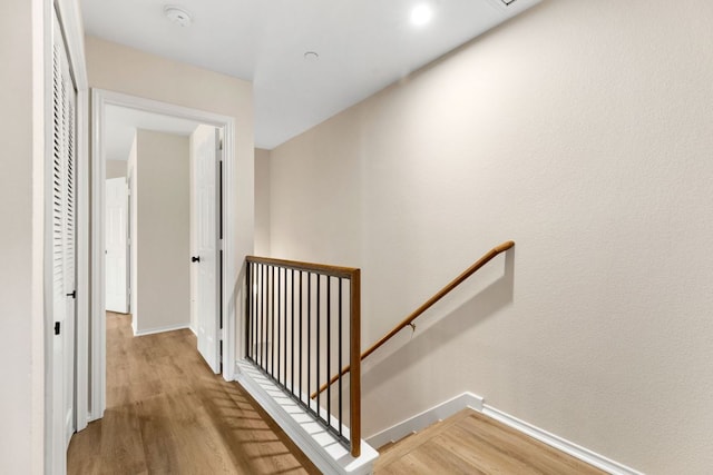 corridor with wood finished floors, baseboards, and an upstairs landing