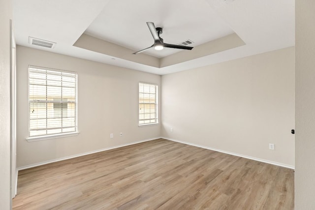 unfurnished room with light wood-type flooring, a ceiling fan, visible vents, and a raised ceiling