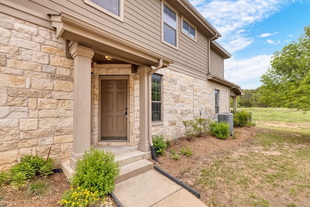 doorway to property featuring stone siding and central AC unit
