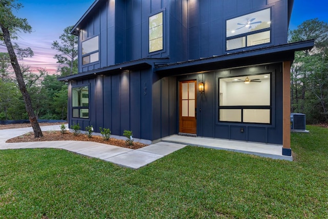view of exterior entry with board and batten siding, a lawn, and cooling unit