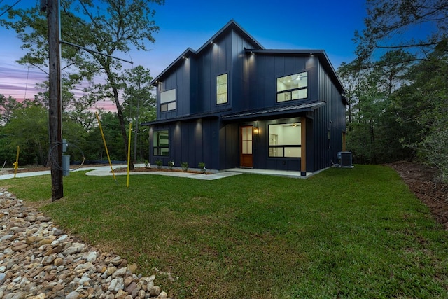 rear view of house with board and batten siding, a lawn, and central AC unit