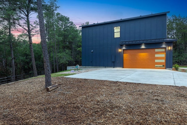 view of property exterior with board and batten siding, a detached garage, concrete driveway, and fence
